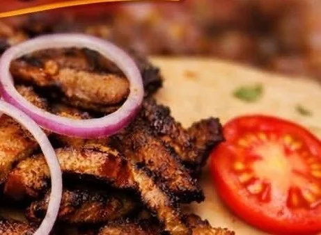Close-up of grilled suya with onion and tomato